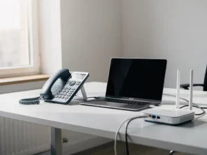 VoIP-bureautelefoon verbonden met laptop op zakelijk bureau, ethernetkabel en router zichtbaar, natuurlijk licht, Belgische kantooromgeving.