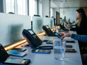 Meerdere smartphones en bureautelefoons die tegelijk oplichten op een modern kantoorbureau, met overlappende signaalgolven zichtbaar in een glas water.